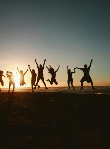 Silhouette of a group of friends jumping on a beach at sunset, expressing joy and freedom.