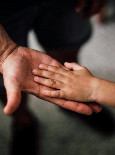 Close-up of a child's hand resting gently on a man's hand, symbolizing love and support.