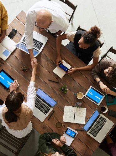 Top view of a diverse team collaborating in an office setting with laptops and tablets, promoting cooperation.