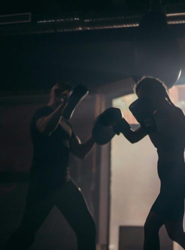 Silhouetted boxers sparring during an intense training session in a dimly lit gym.