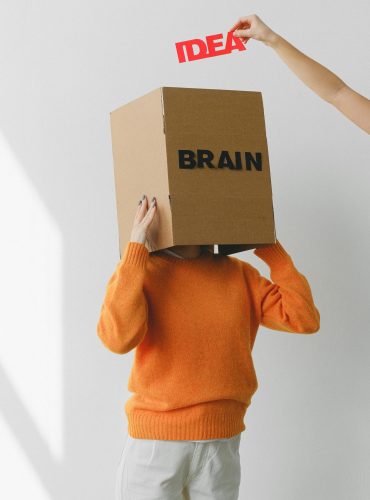 Crop person putting Idea title in cardboard box with Brain inscription on head of female on light background